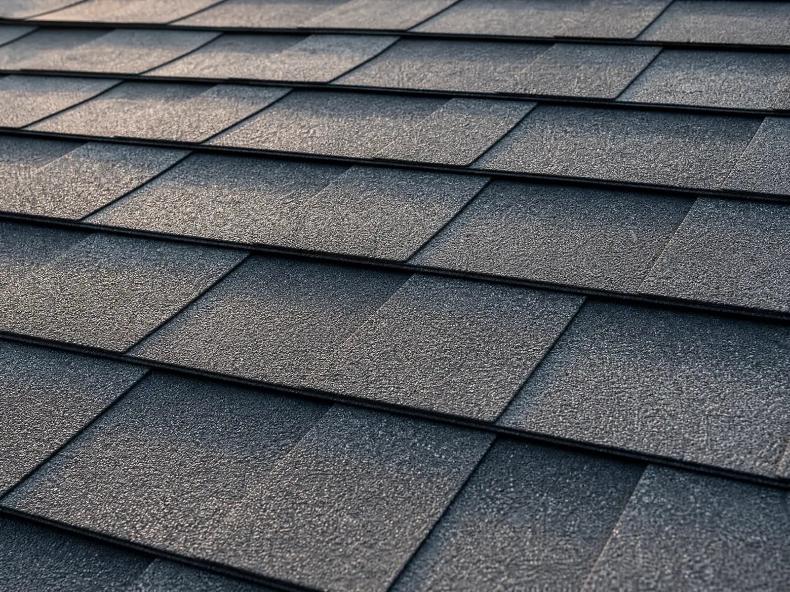 Close-up of overlapping dark gray architectural asphalt shingles in low evening light