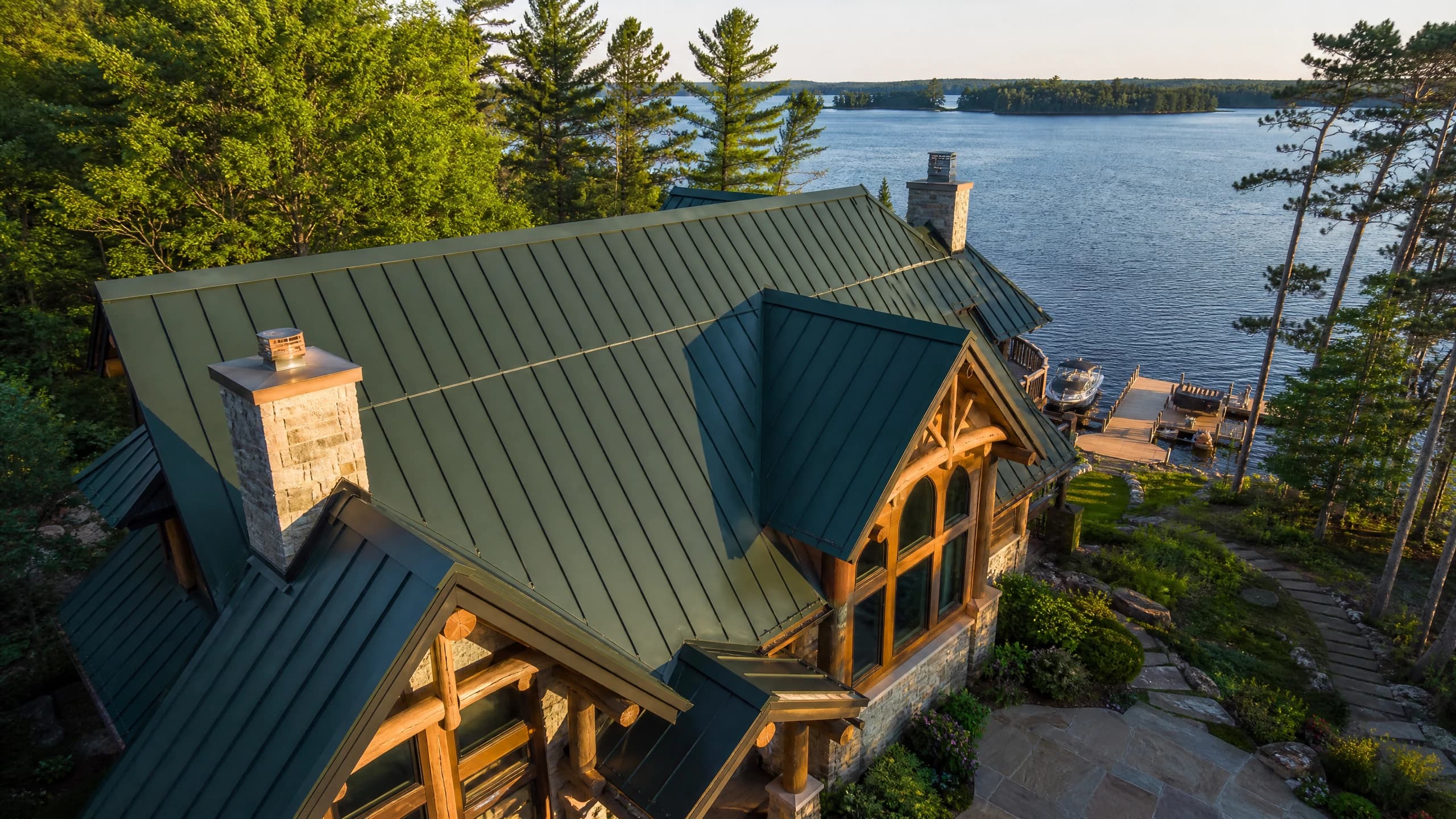 Luxury timber-frame chalet on the Whitefish Chain with a forest-green standing seam metal roof, private dock and open water beyond — Silver Loon Roofing