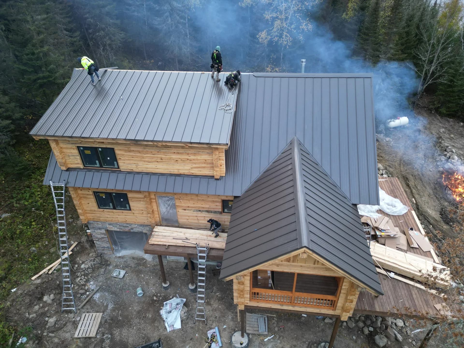 Roofing crew installing charcoal-gray standing seam metal panels on a timber-frame lodge in northern Minnesota lake country