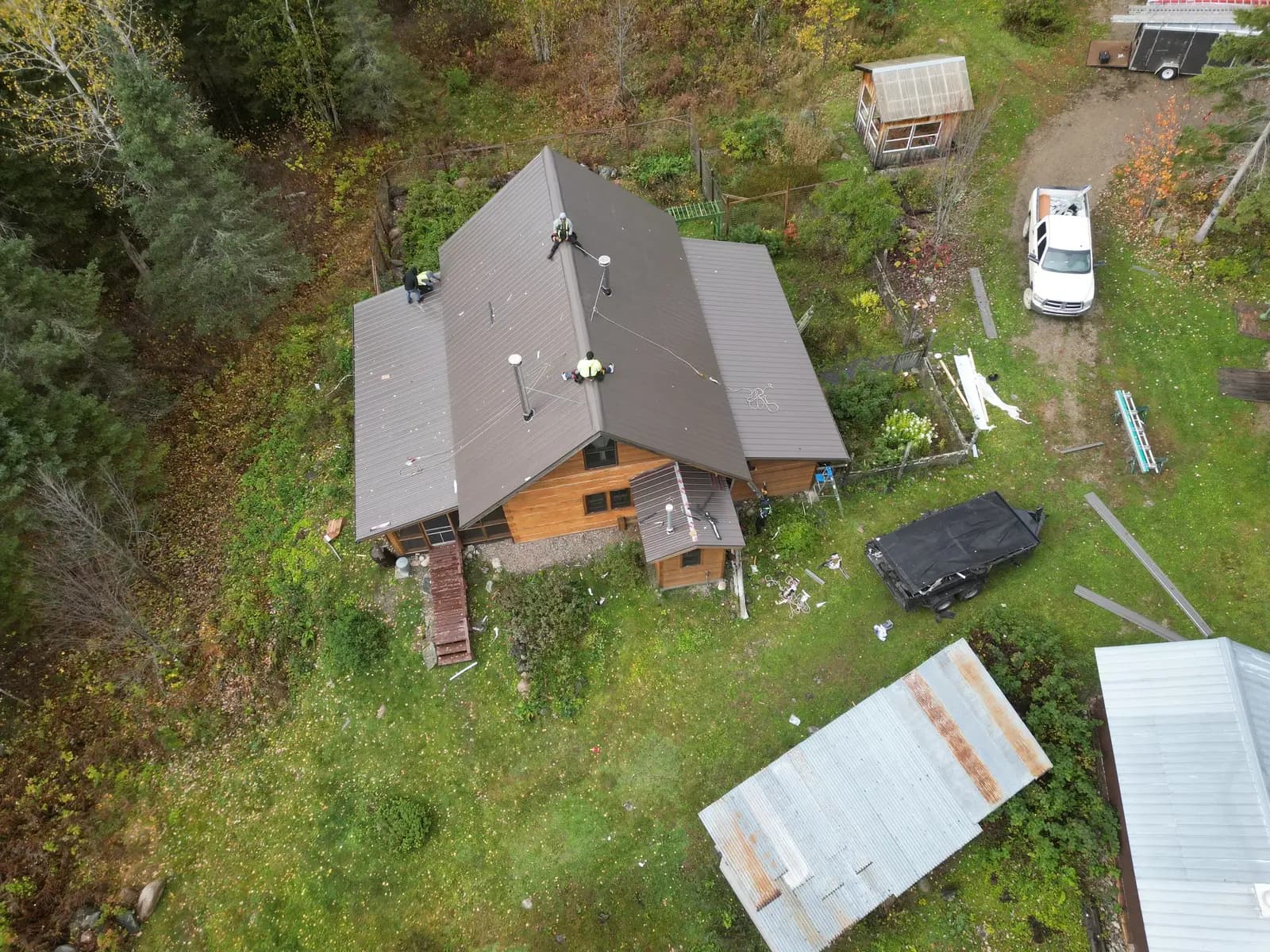 Steep A-frame log cabin with a new gray-brown standing seam metal roof, crew working at the ridge