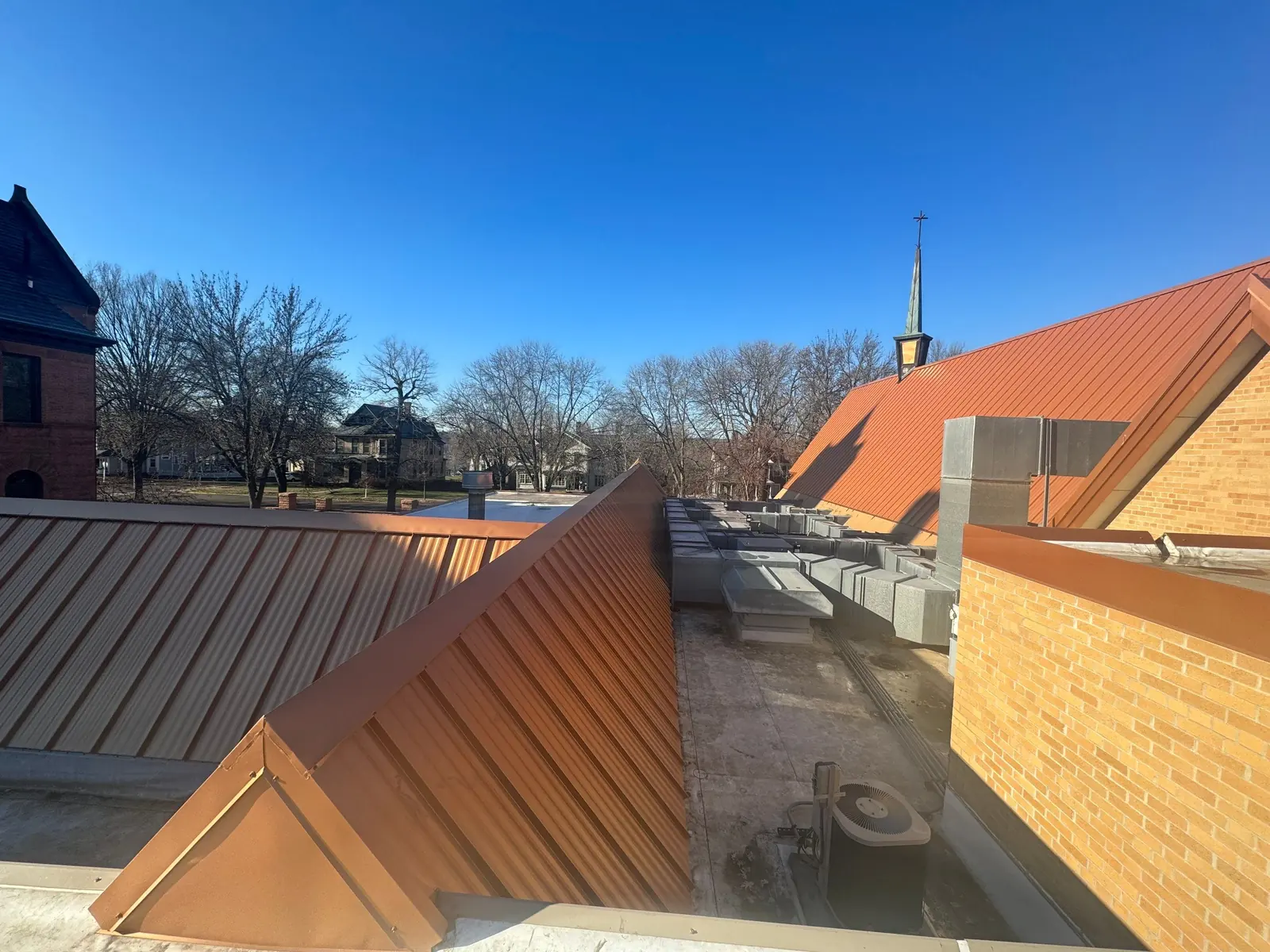 Wide plane of a copper-orange standing seam roof on a brick church