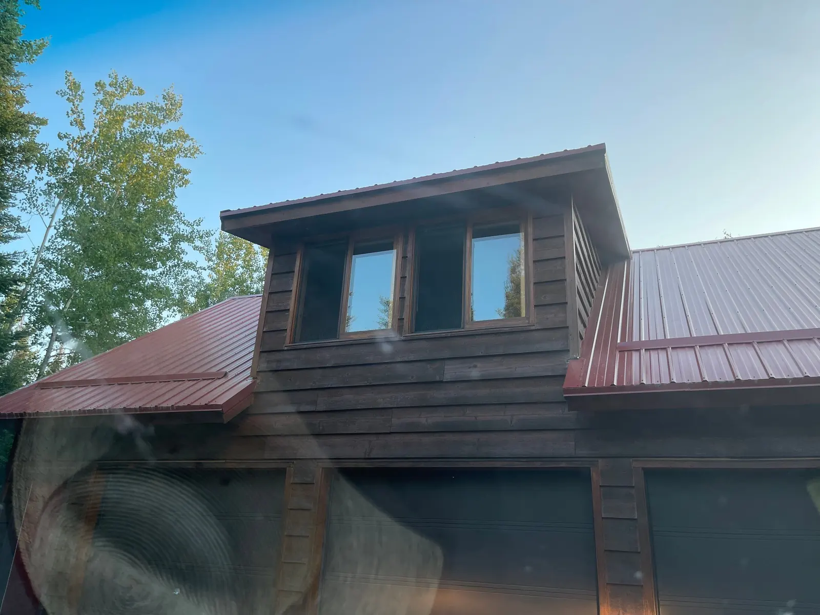 Wide view of a dark log cabin with multiple gables and barn-red standing seam roof