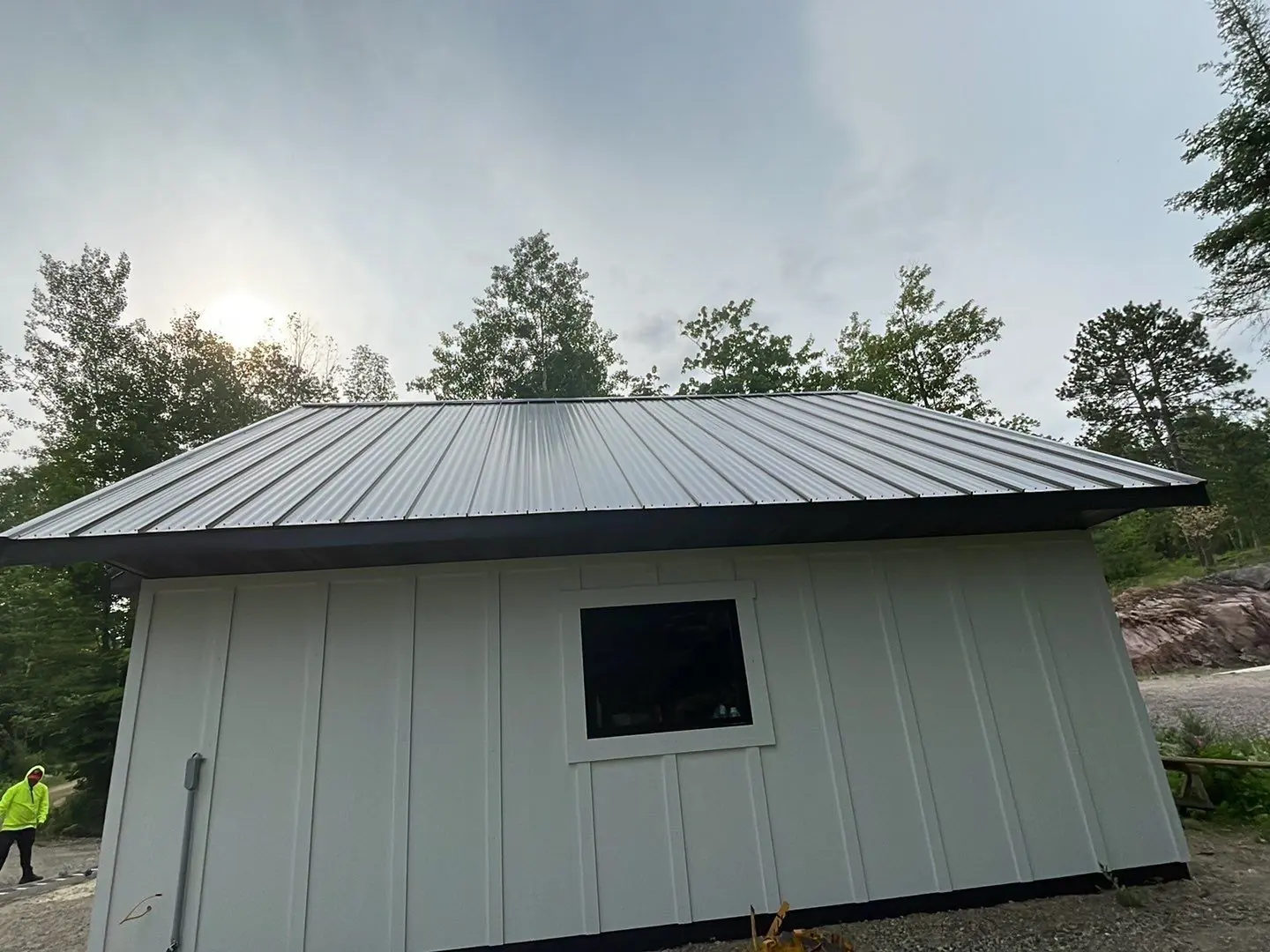 Small white board-and-batten outbuilding with dark bronze standing seam roof on a granite rock outcrop