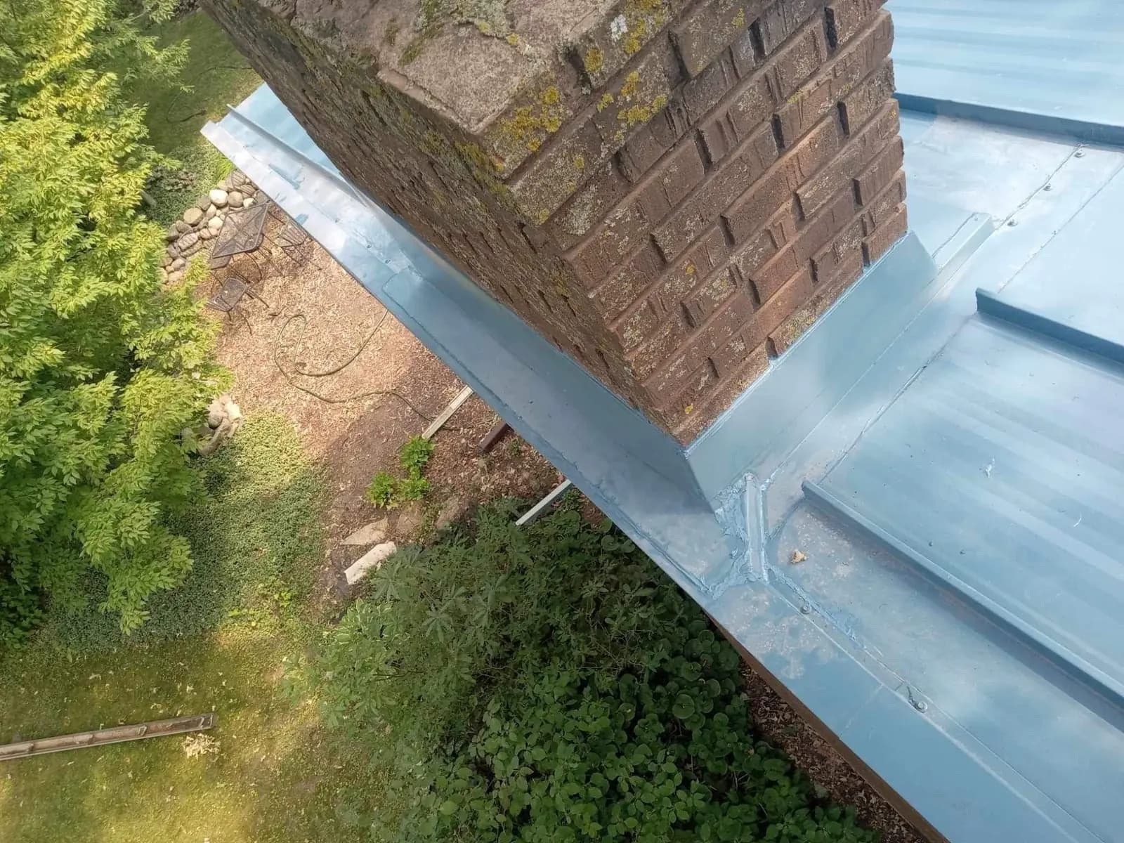 Looking up from the ground at a blue standing seam roof and brick chimney corner