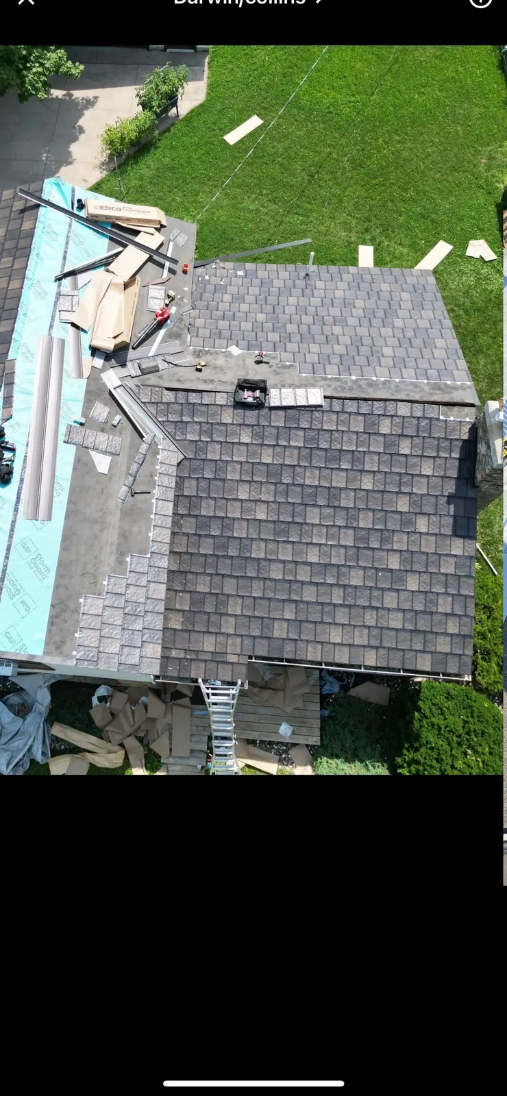 Aerial view of a synthetic slate-style shingle roof mid-install, underlayment and staged bundles visible