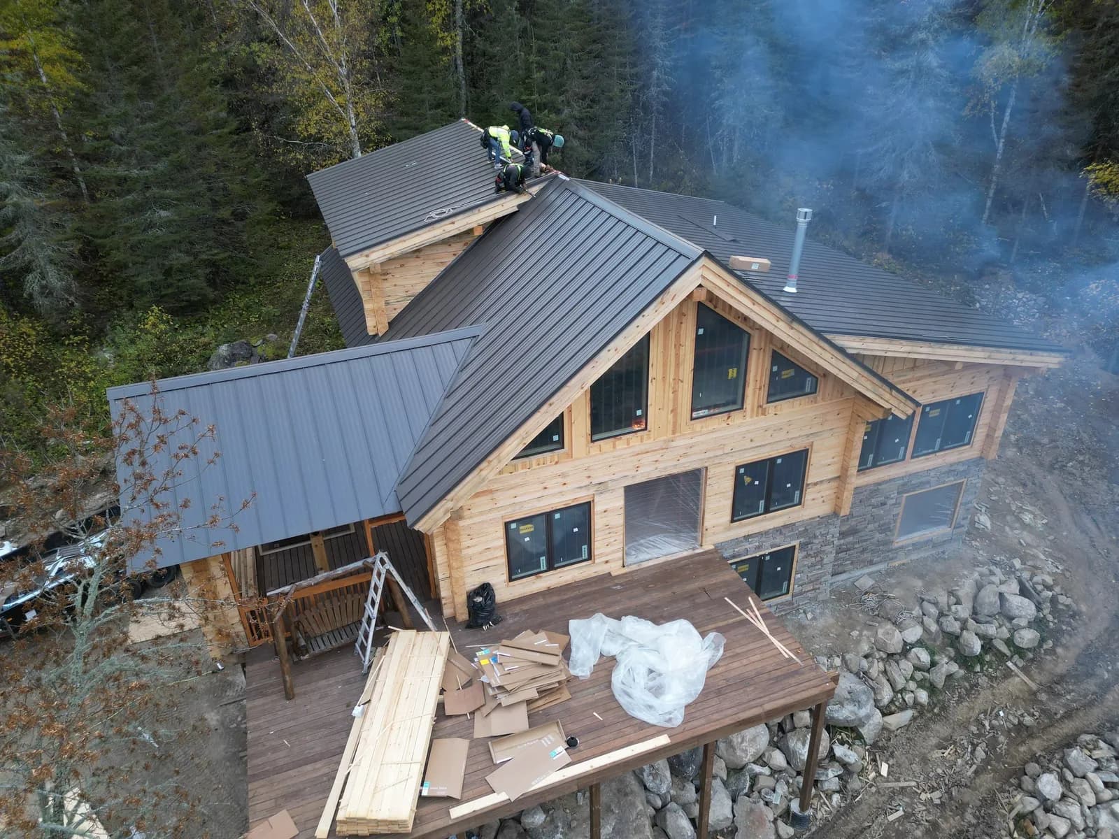 Three crew members tied off on the ridge of a timber-frame lodge roof near Crane Lake, installing standing seam metal panels