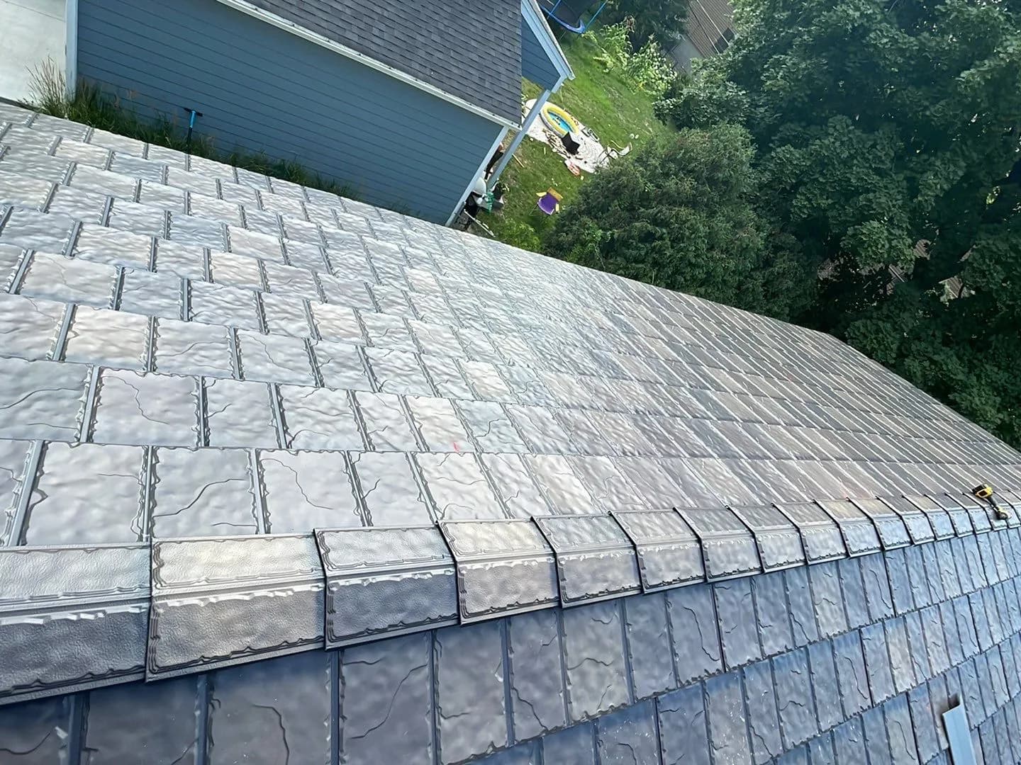 Crew installing synthetic slate roof tiles on a two-story home in Edina, Minnesota, blue sky, backyard with a play area below, August 2023