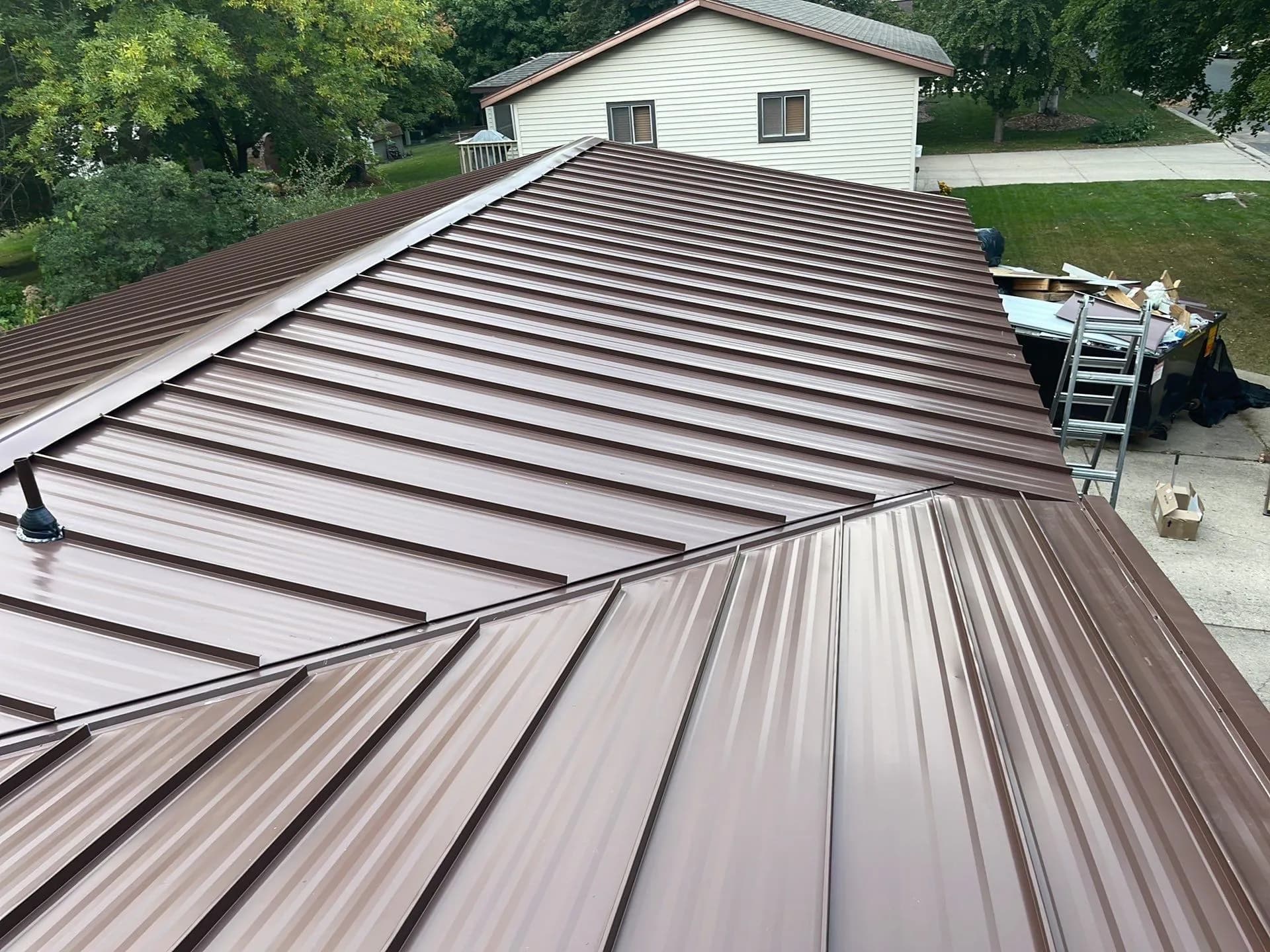 Finished bronze-brown standing seam metal roof valley and brick chimney detail on a ranch-style home in Hutchinson, Minnesota, September 2023
